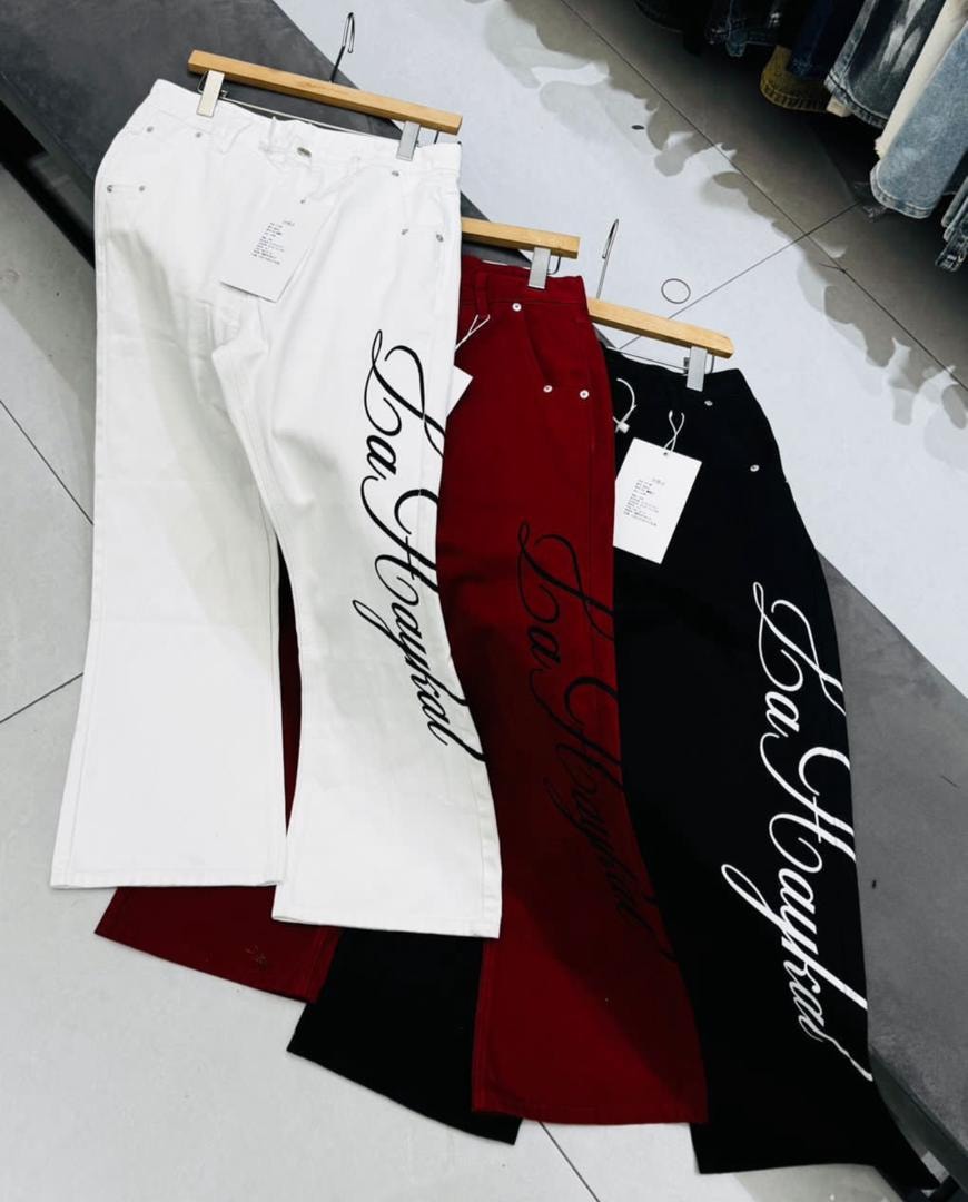 White, red, and black baggy jeans with cursive prints laid out together on a surface.