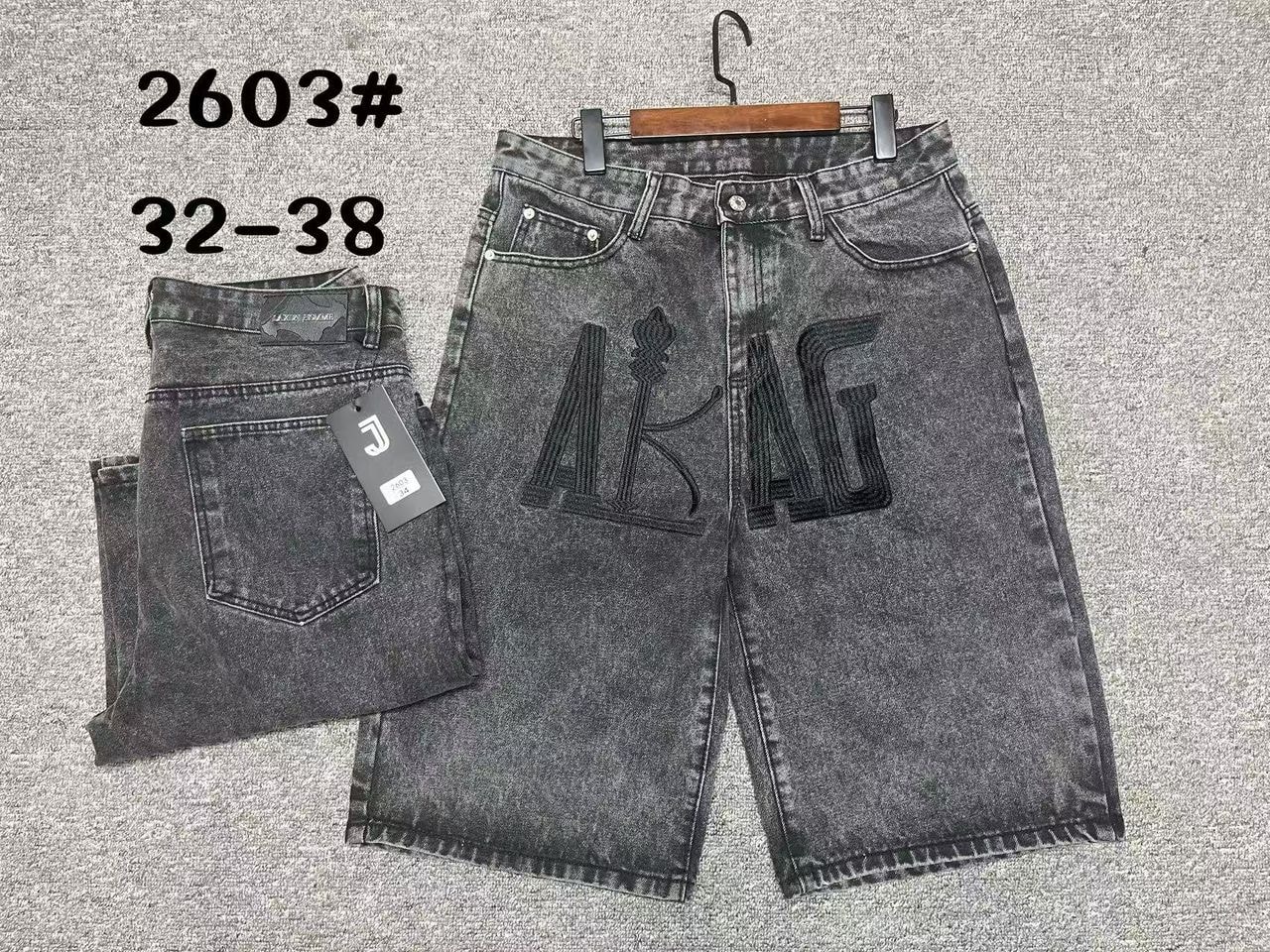 Black acid wash denim jorts with large black embroidery on front leg, shown on hanger and folded back view.