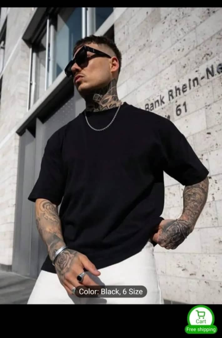 Tattooed model wearing black oversized crewneck t-shirt with white trousers outdoors.