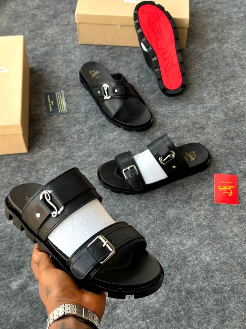 Christian Louboutin black slides held in hand displaying thick sole and buckle hardware.