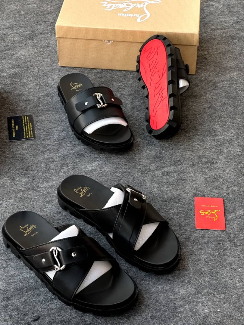 Black Christian Louboutin slides with silver buckle and red sole beside branded box and cards.