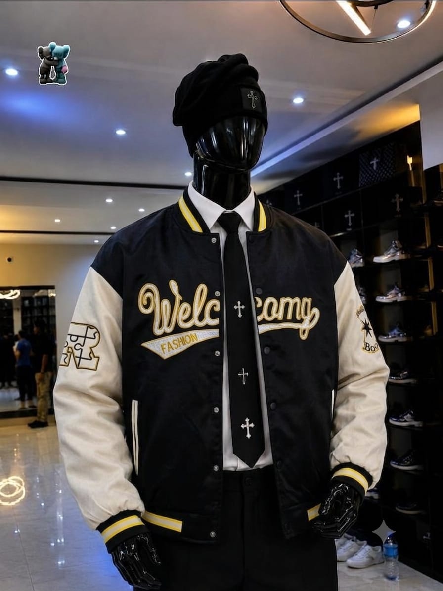 Mannequin styled in black and cream varsity jacket with yellow accents, gold embroidery, beanie, shirt and tie.