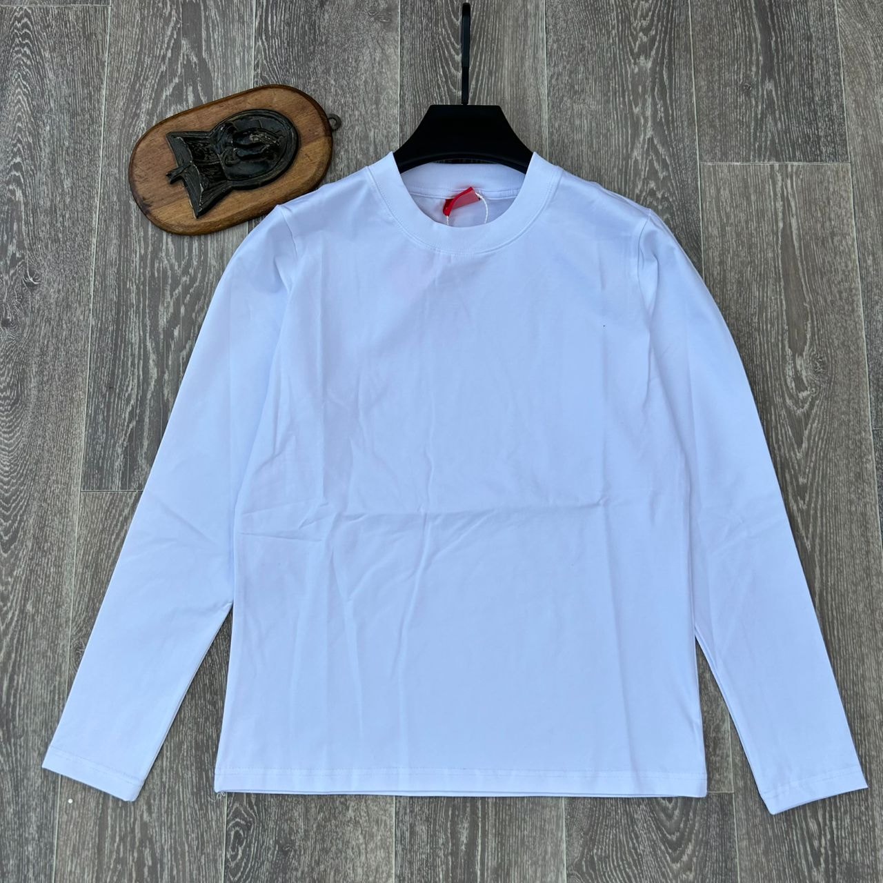 White plain body hug long sleeve top on hanger against wooden background.
