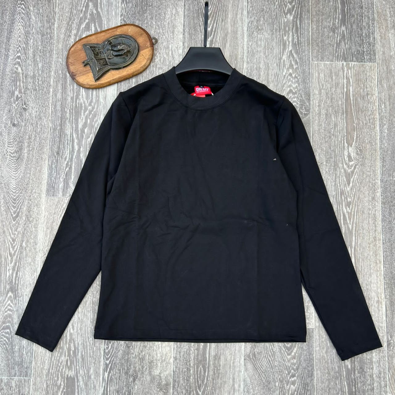 Black plain body hug long sleeve top on hanger against wooden background.