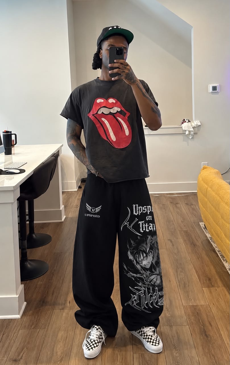 Man wearing black Upspeed graphic joggers with anime and text prints, styled with Rolling Stones t-shirt and cap.