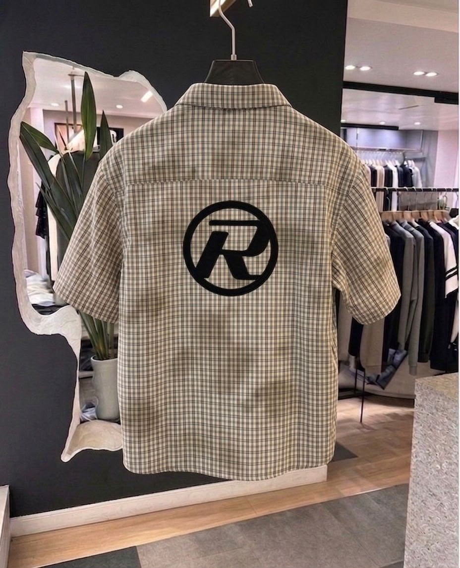 Back view of beige plaid short sleeve shirt showing large circular black logo print.