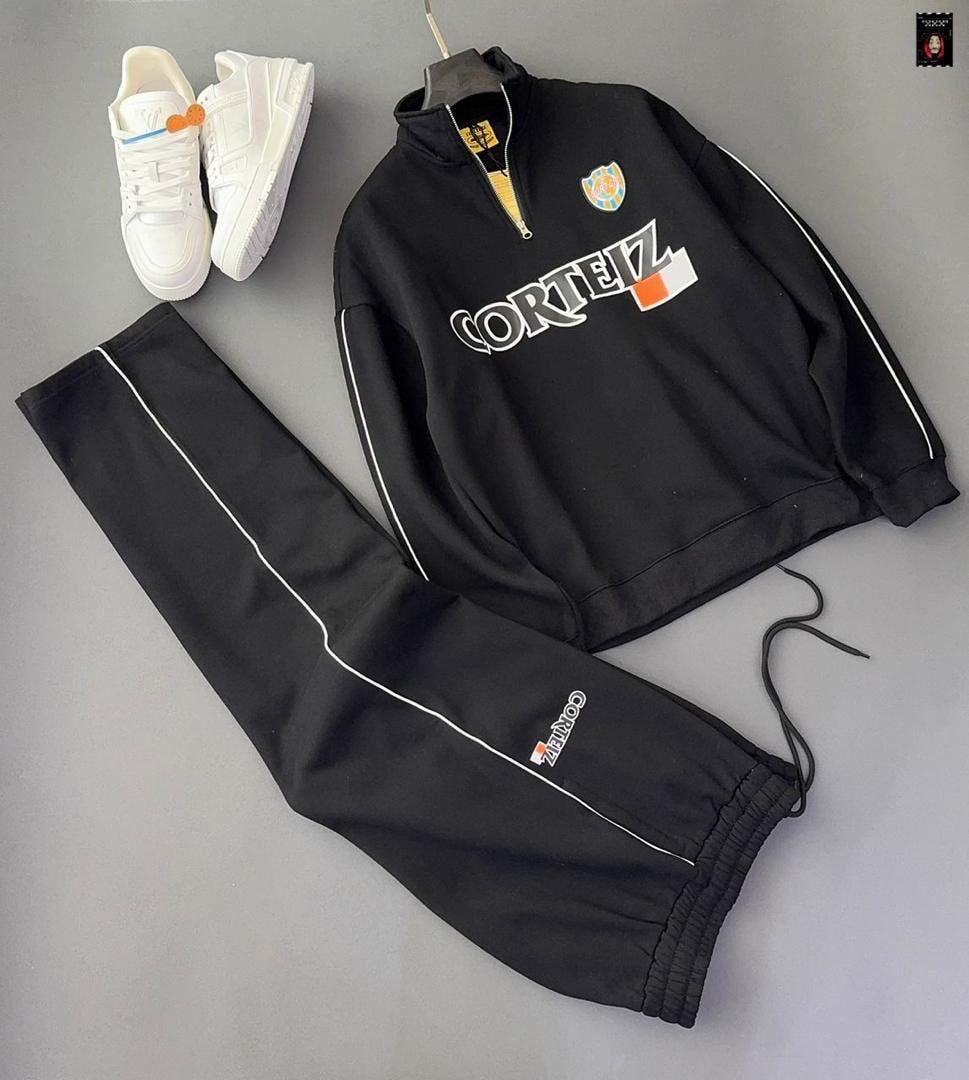 Black Corteiz quarter-zip sweatshirt and jogger pants with white stripes, flat lay with sneakers.