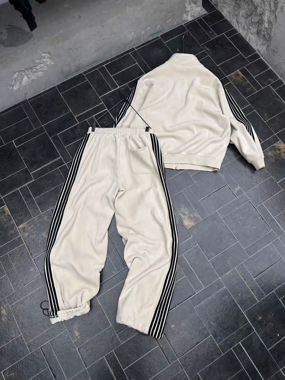 Flat lay of cream velour tracksuit set with black stripes on tiled floor.