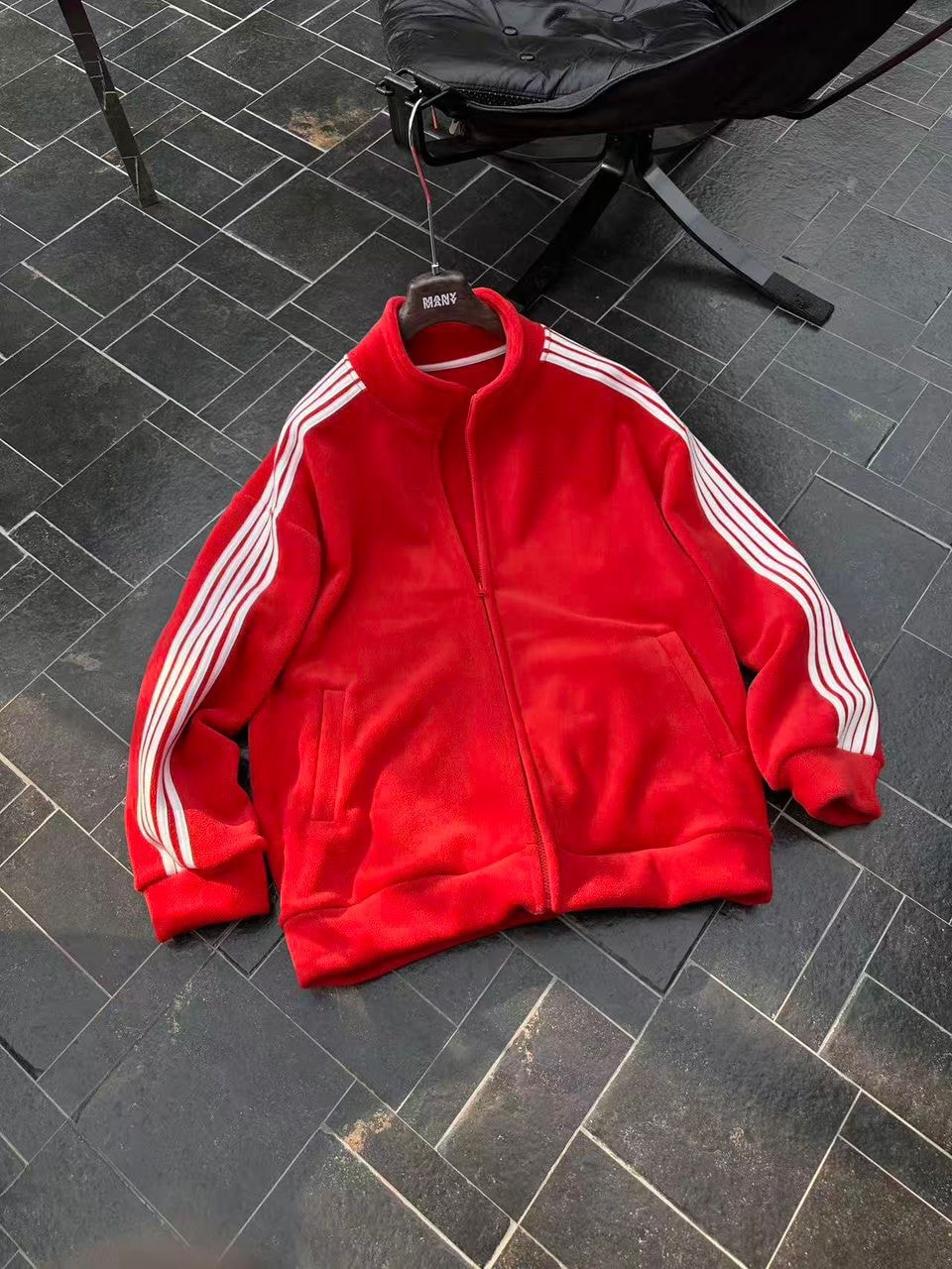 Red velour zip-up jacket with white stripes hanging on chair.