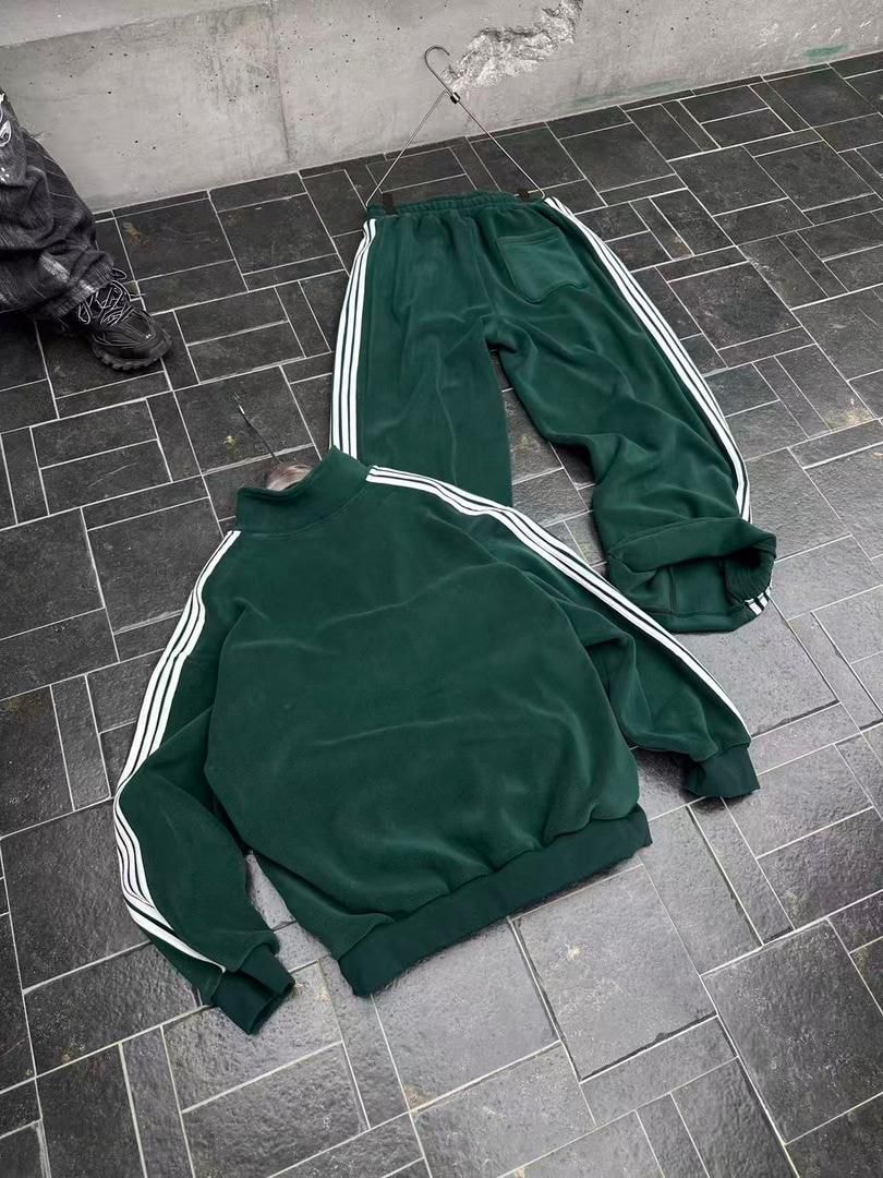 Flat lay of green velour tracksuit top and pants with white stripes.