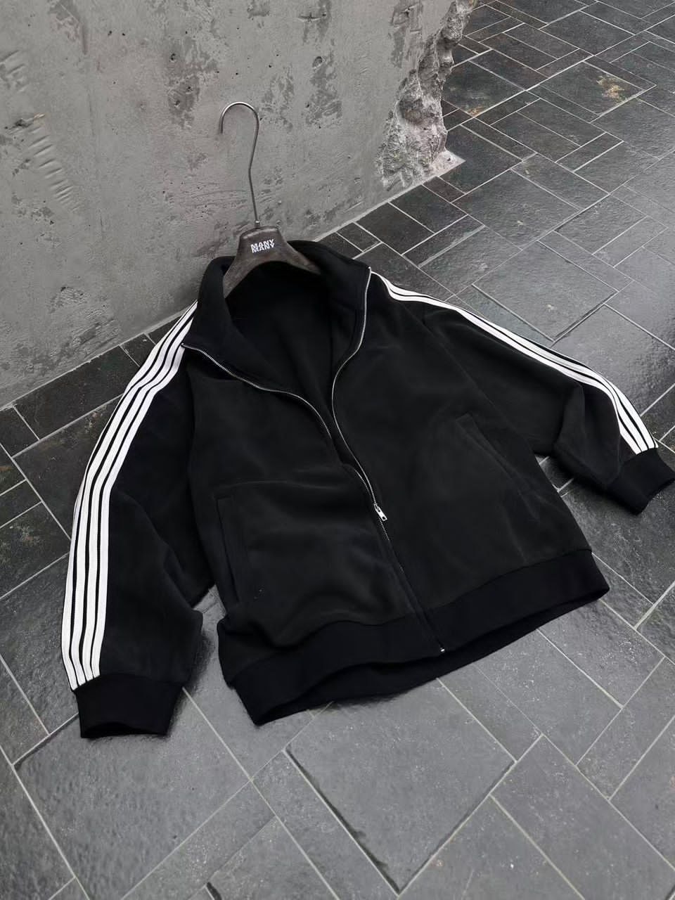 Flat lay of black velour zip-up jacket with white stripes and pockets.