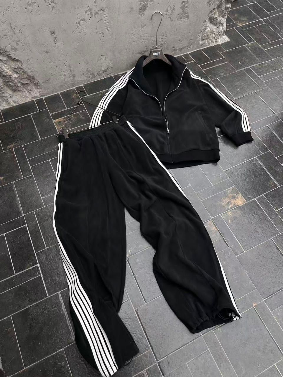 Flat lay of black velour tracksuit set including jacket and pants with white stripes.