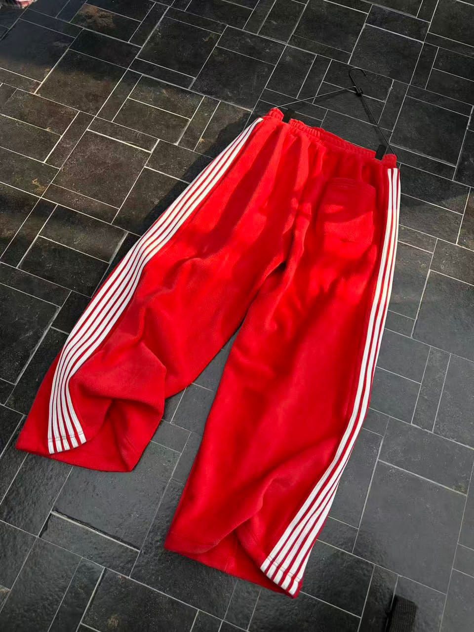 Flat lay of red velour tracksuit pants with white side stripes on tiled floor.