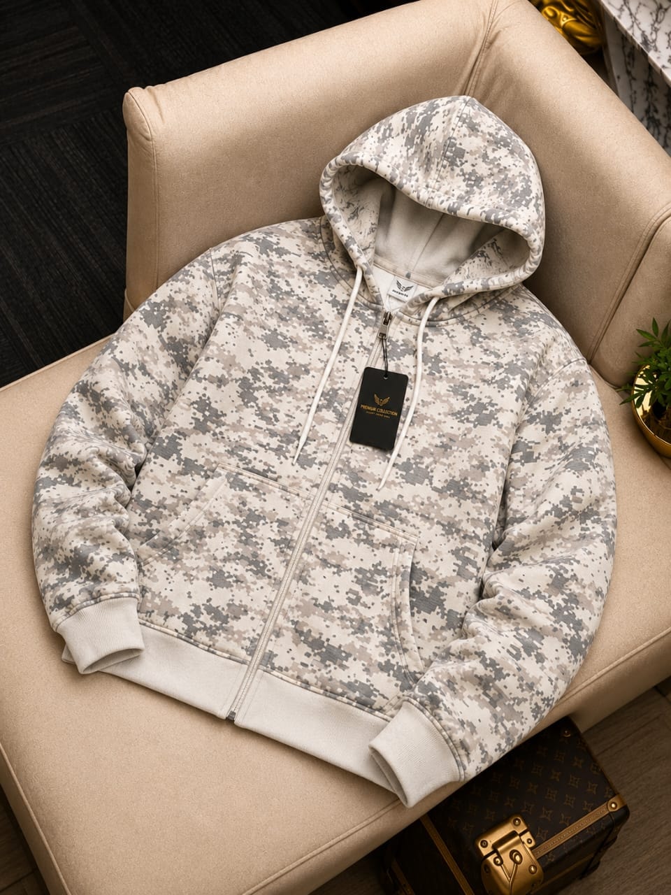 Cream digital camouflage zip-up hoodie on a beige chair, showing front view with hood up and black tag.