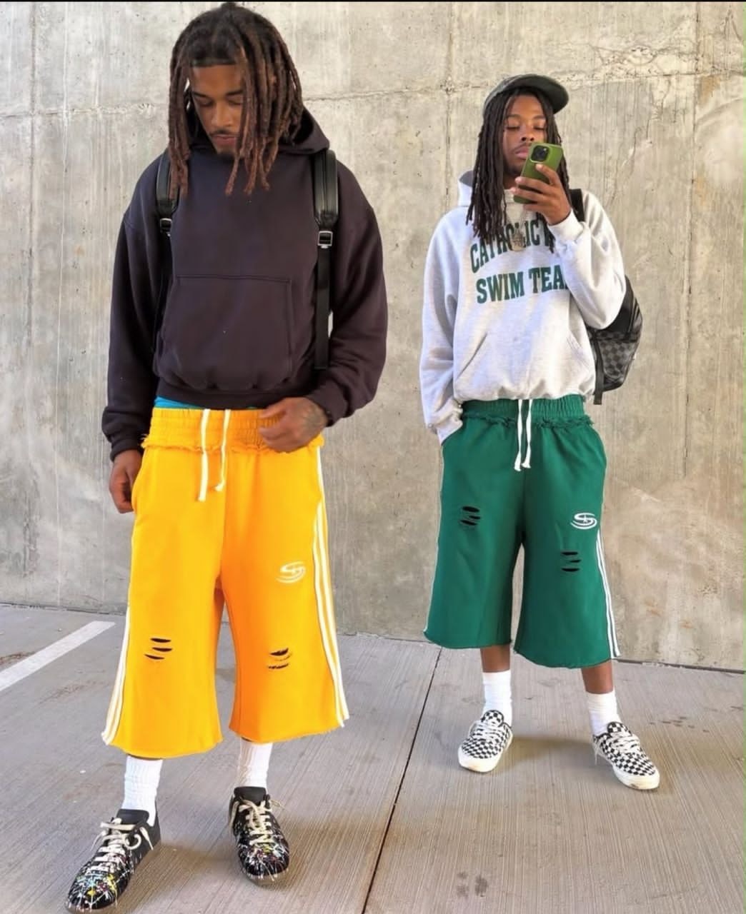 Two models wearing yellow and green distressed striped wide-leg shorts with hoodies.