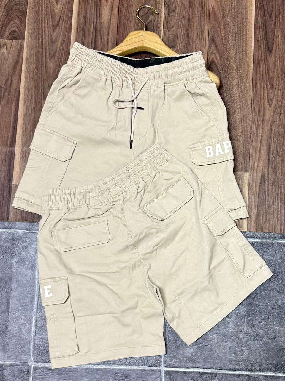 Beige BAPE cargo shorts on hanger showing front and back with side logo patches.