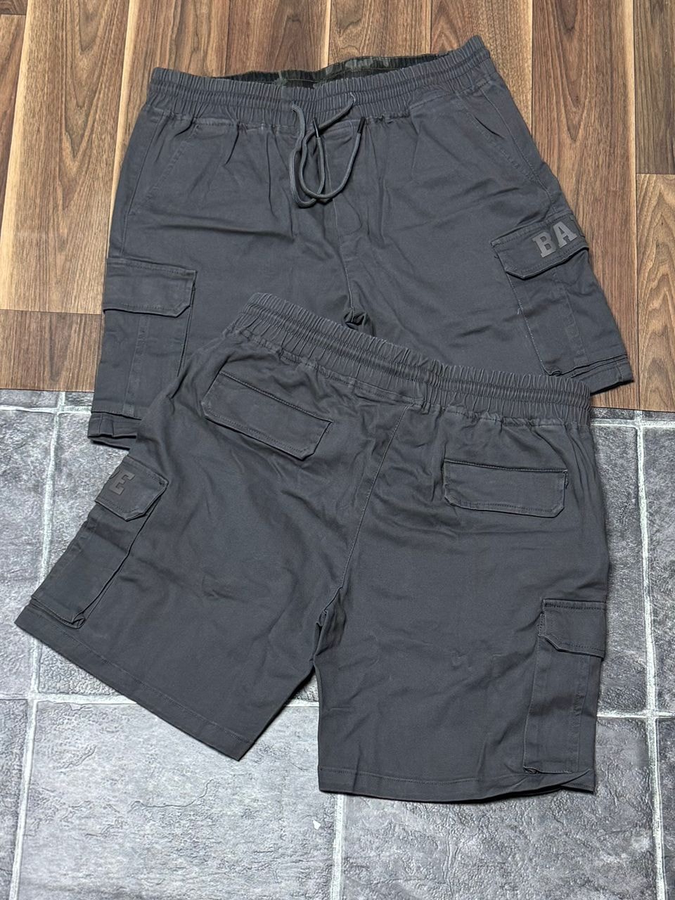 Gray BAPE cargo shorts displayed from multiple angles on wooden surface.
