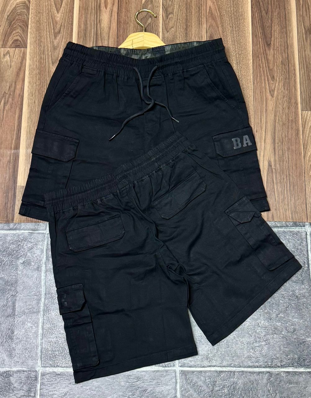 Black BAPE cargo shorts shown in front and back views on tiled floor.
