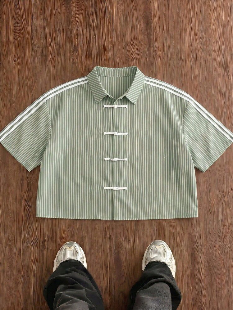 Flat lay view of green striped short sleeve shirt with frog buttons on wooden floor.