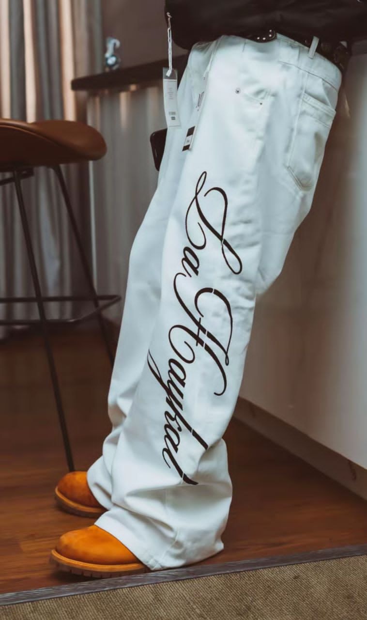 Model wearing white La Haykal jeans with black cursive script on the leg.