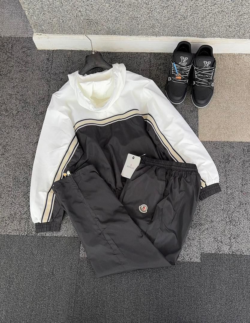 White and black hooded tracksuit with beige stripes laid flat on carpet with black LV sneakers and Moncler tag visible.