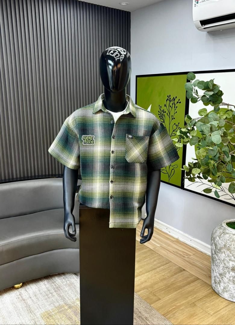 Mannequin wearing green and yellow plaid short sleeve button-down shirt with chest pocket.