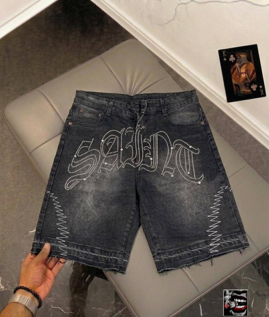Back view of dark denim jorts with large white rhinestone 'SERPENT' lettering and zigzag side seam details.