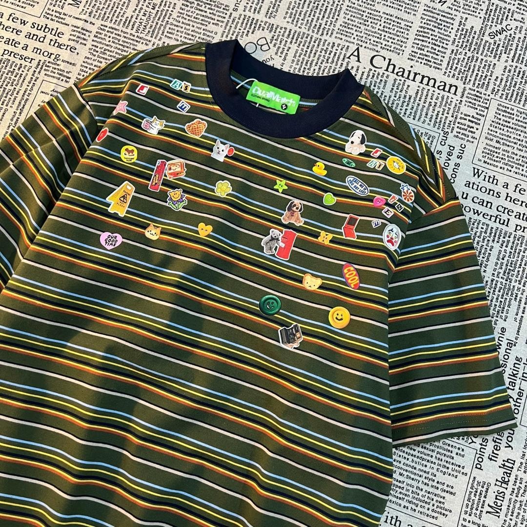 Olive striped polo shirt with multicolored stripes, cartoon patches and navy collar on newspaper background.