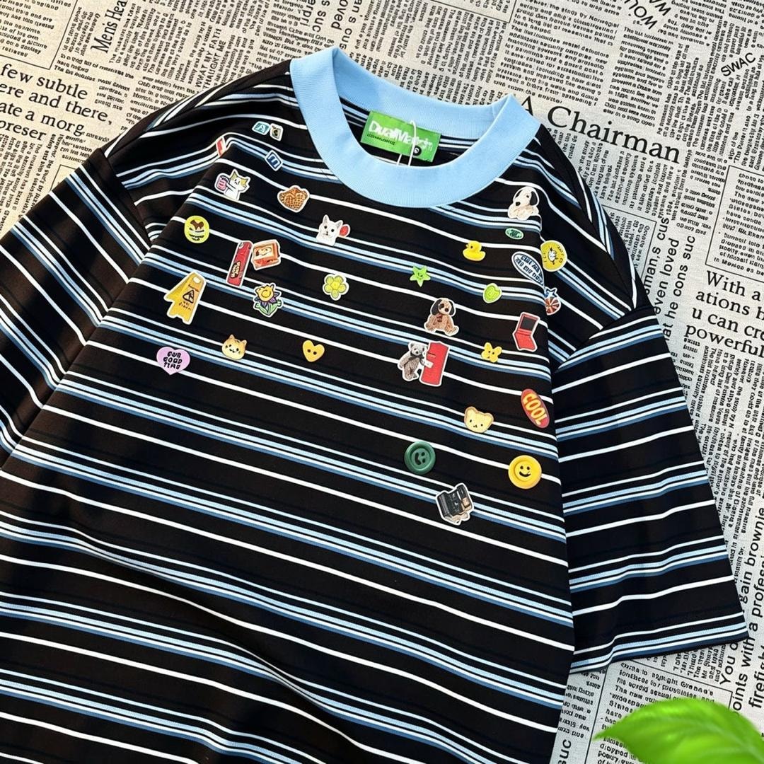 Black striped polo shirt with cartoon patches and light blue collar on newspaper background.