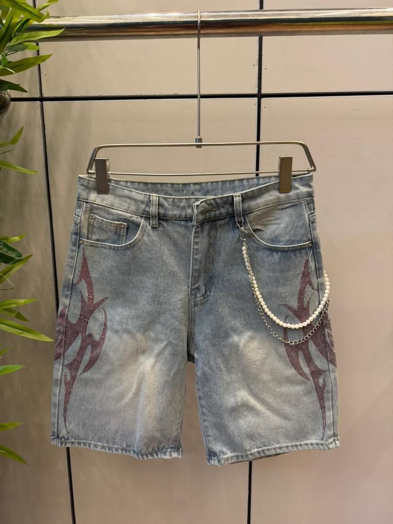 Light blue denim jorts with red flame embroidery and pearl chain displayed on metal hanger.