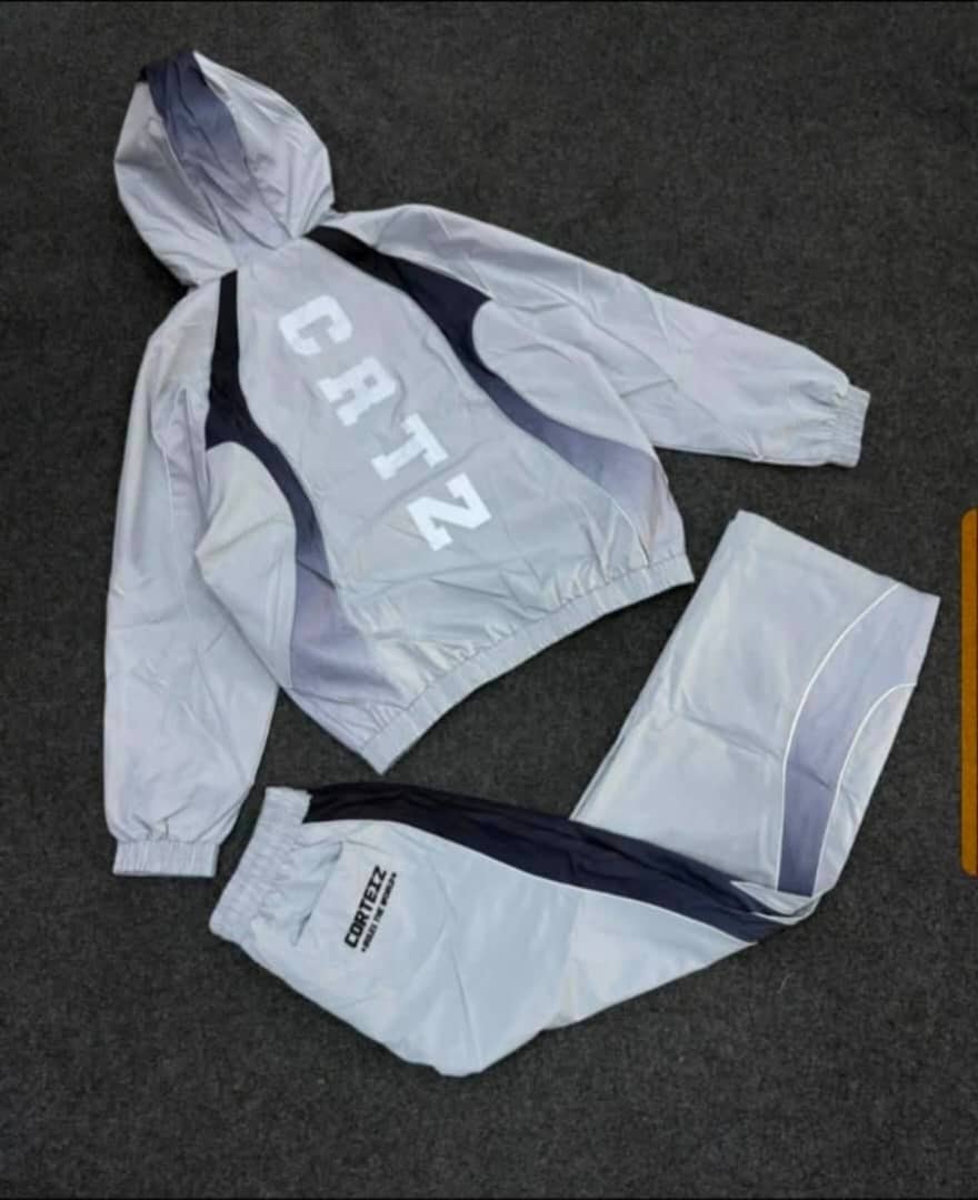 Cortz hooded tracksuit set in white and navy laid flat, showing jacket with large back branding and matching pants.