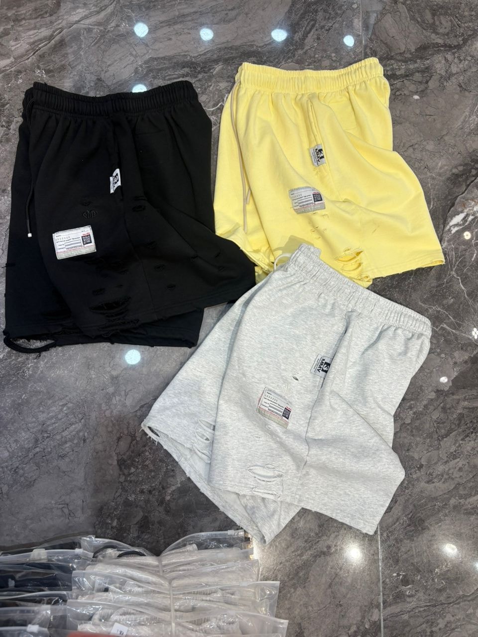 Black, yellow, and gray distressed shorts with rips and patches laid on marble surface.