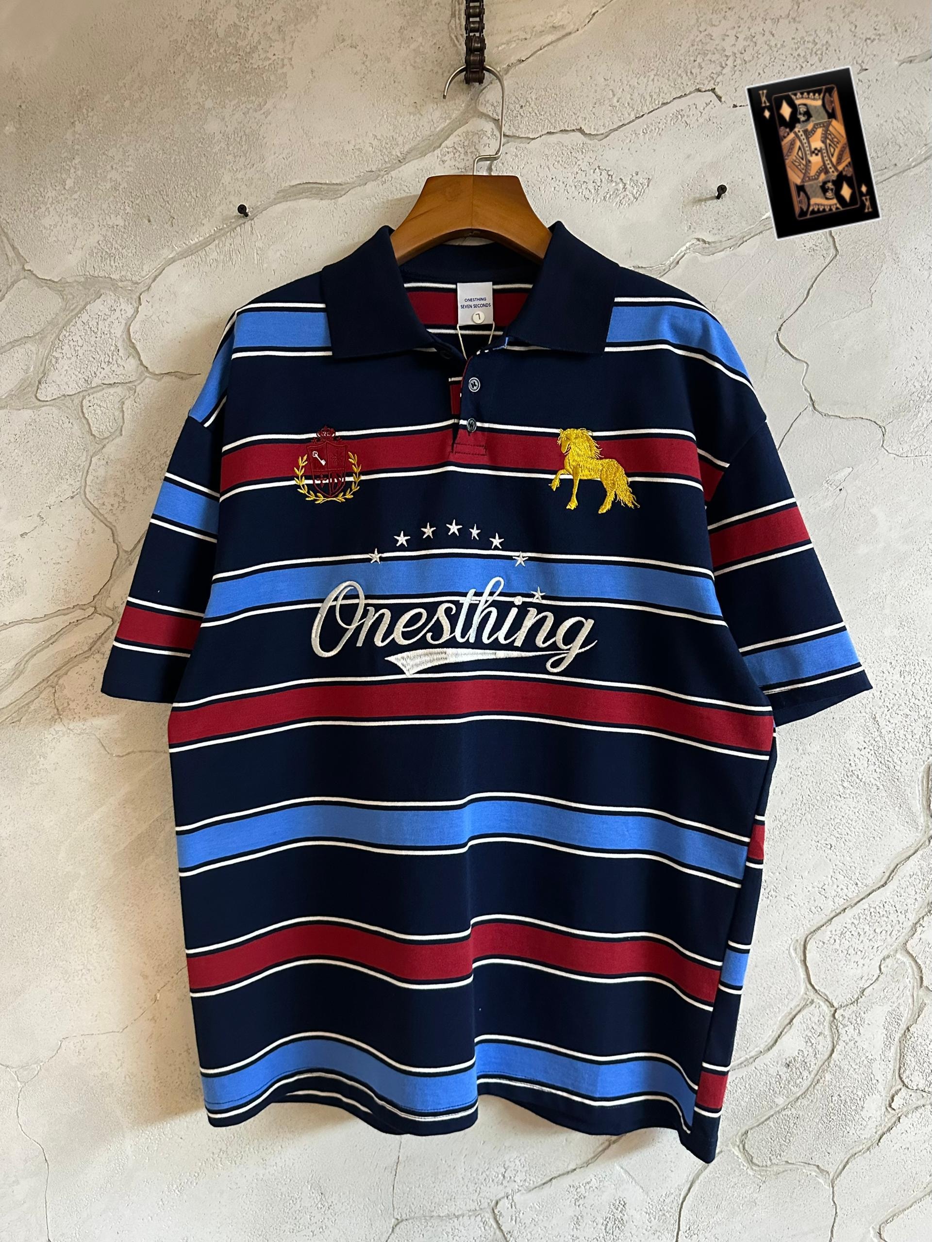 Onesthing navy striped embroidered polo hanging on wooden hanger against wall with playing card.