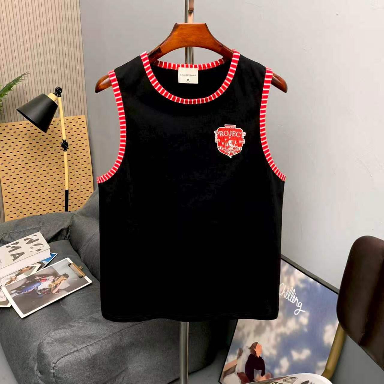 Black armless tank top with red striped trim and chest logo on wooden hanger.