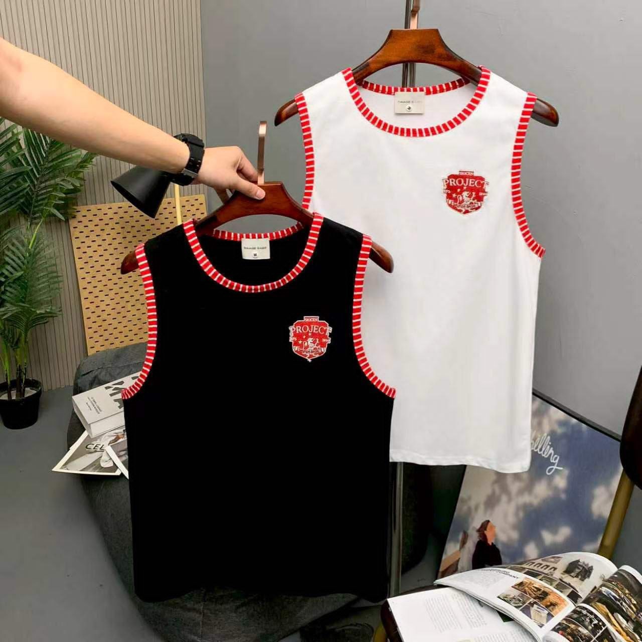 Black and white sleeveless armless tops with red trim and logo on wooden hangers.