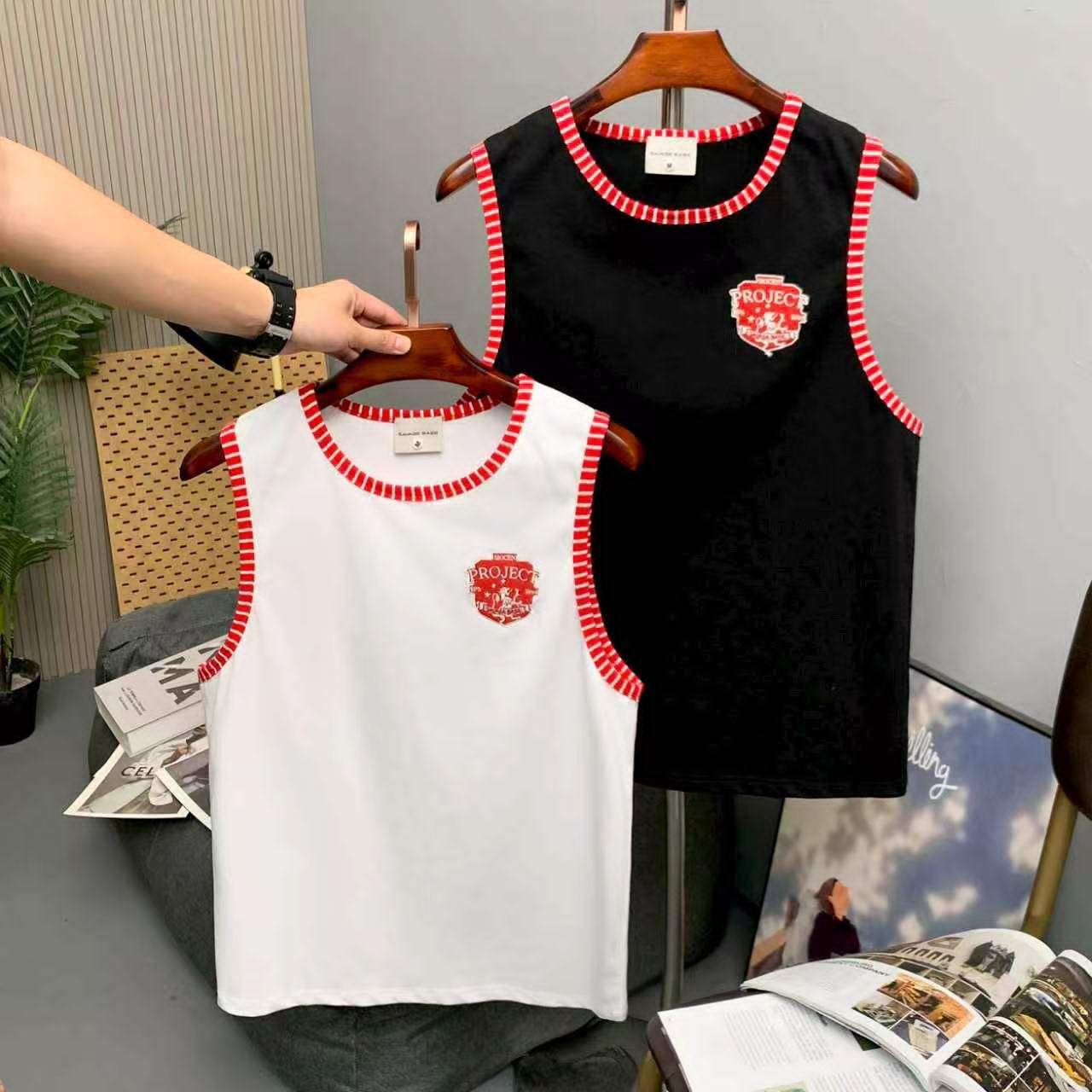 White and black armless tops with red striped trim held on hangers in studio setting.