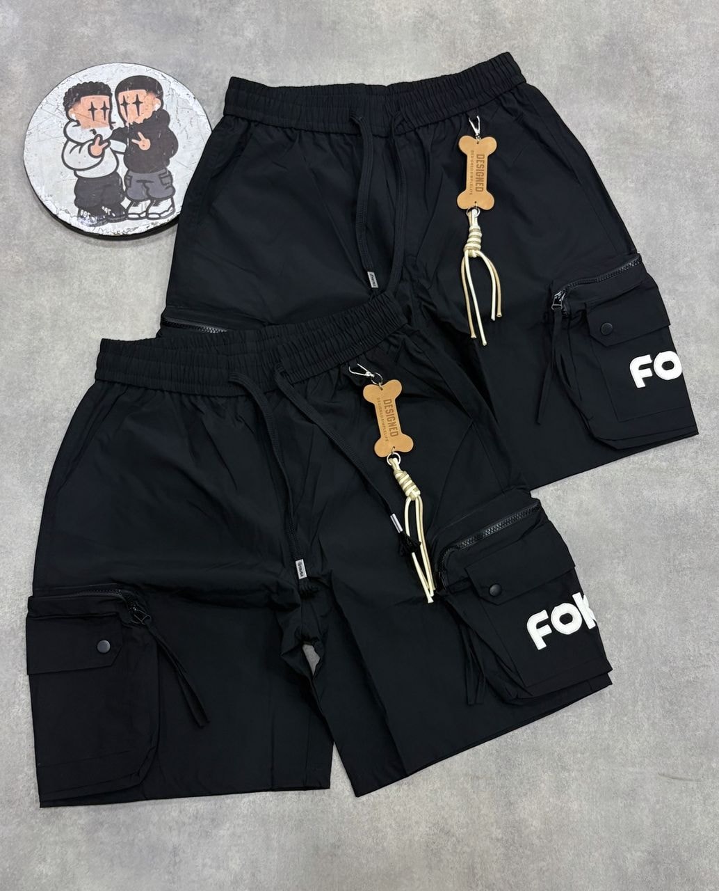 Black and khaki combat cargo shorts with FOF print, bone keychains, and circular sticker.