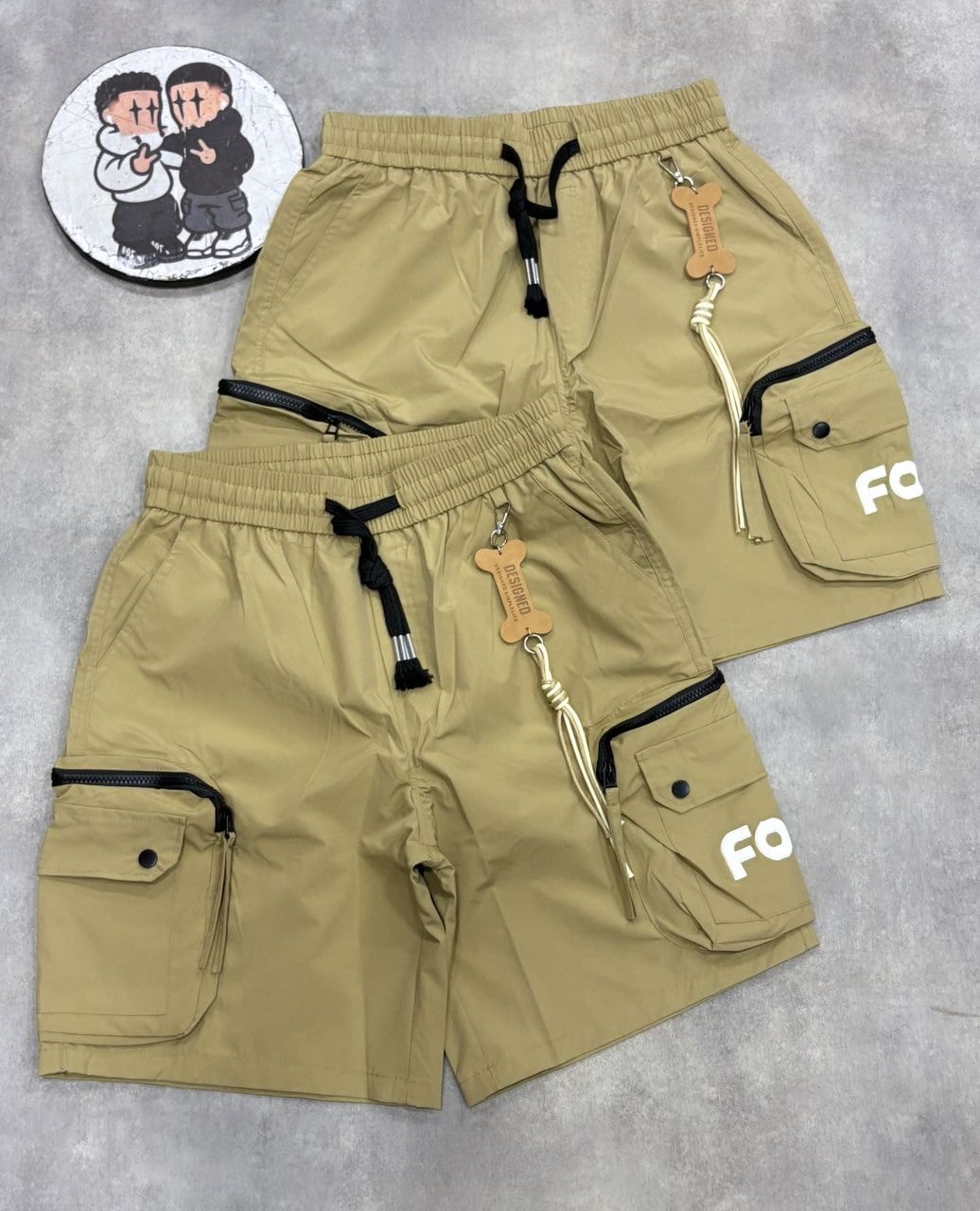 Khaki and black combat cargo shorts with FOF print, keychain details, and cartoon sticker.