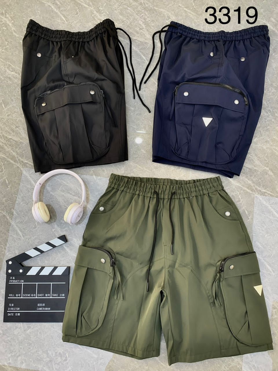 Black, navy, and olive combat cargo shorts flat lay with headphones and clapperboard.