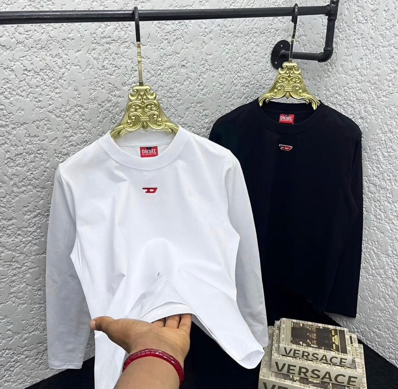 White and black Diesel long sleeve body hug tops displayed on decorative hangers showing front view with red logo.
