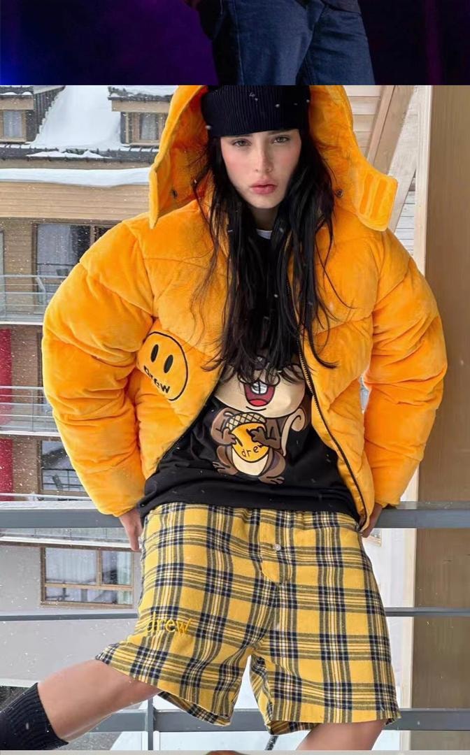 Model wearing yellow Drew puffer jacket outdoors with plaid shorts.