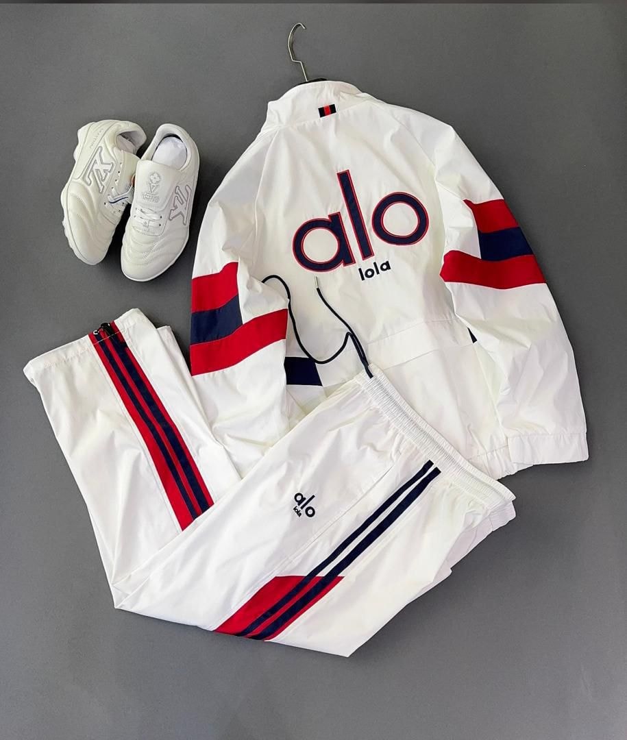 White Alo tracksuit with red and navy stripes shown with white sneakers on gray surface.