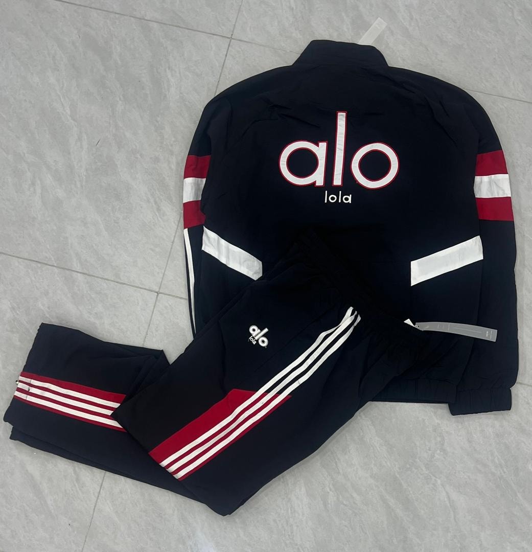 Black Alo tracksuit jacket and pants with red and white stripes laid flat on tiled floor.
