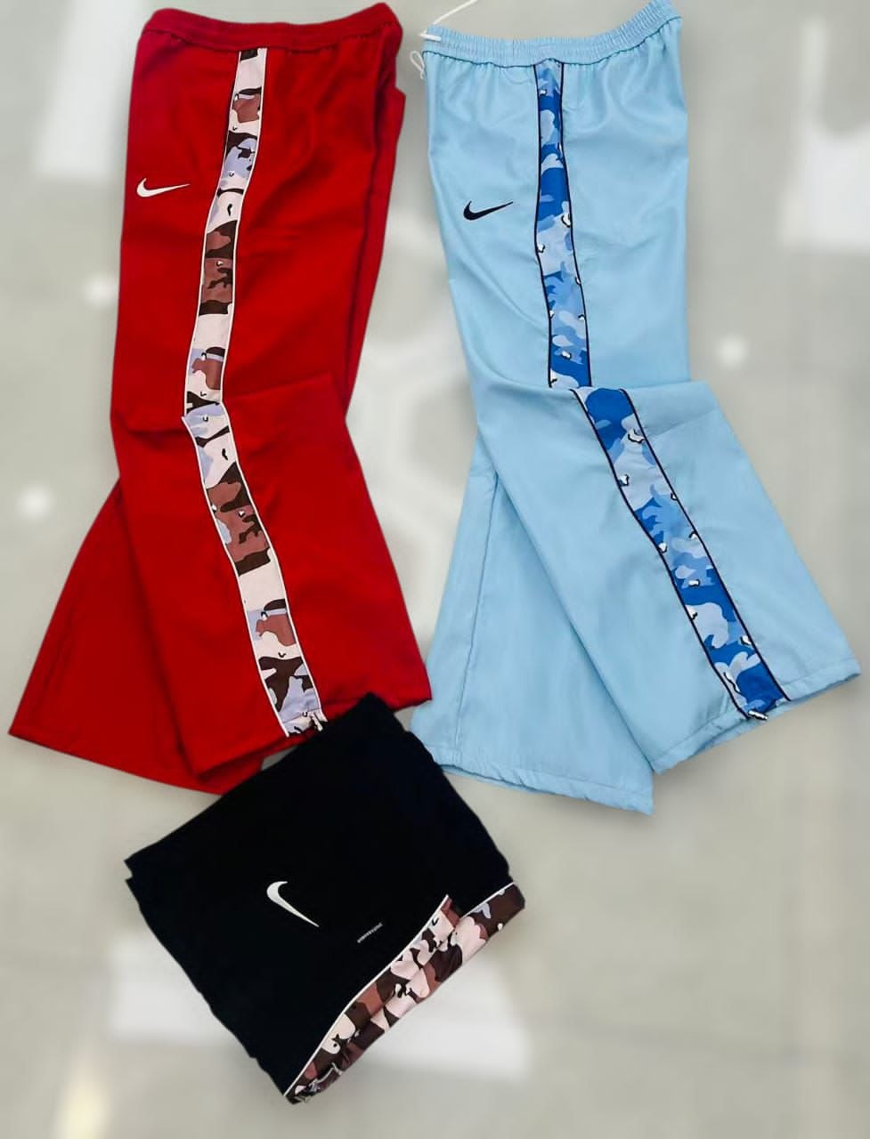 Nike joggers in red, light blue, and black with camouflage side stripes, shown from multiple angles.