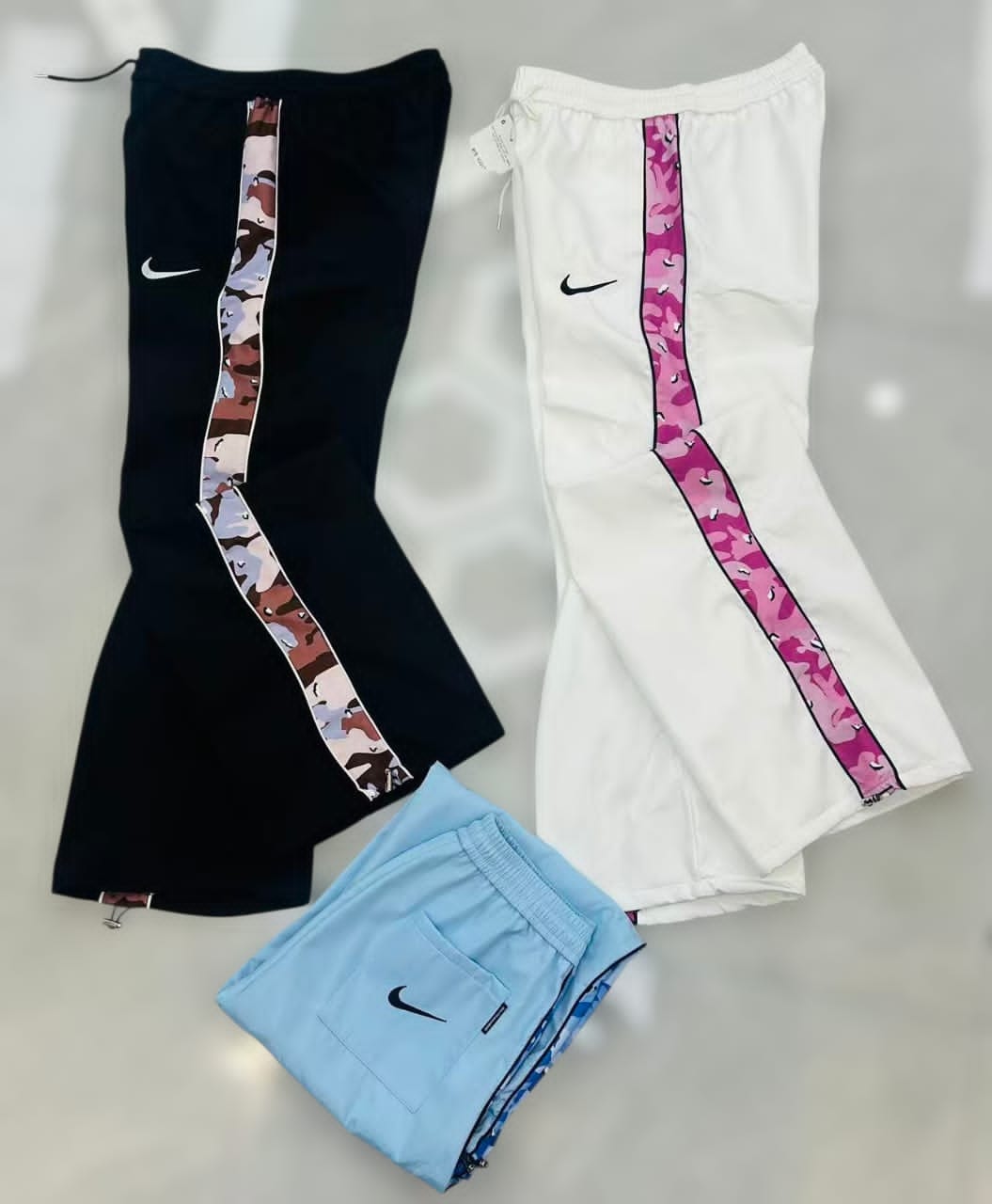 Nike joggers in black, white, and light blue with matching camouflage side stripes laid flat.