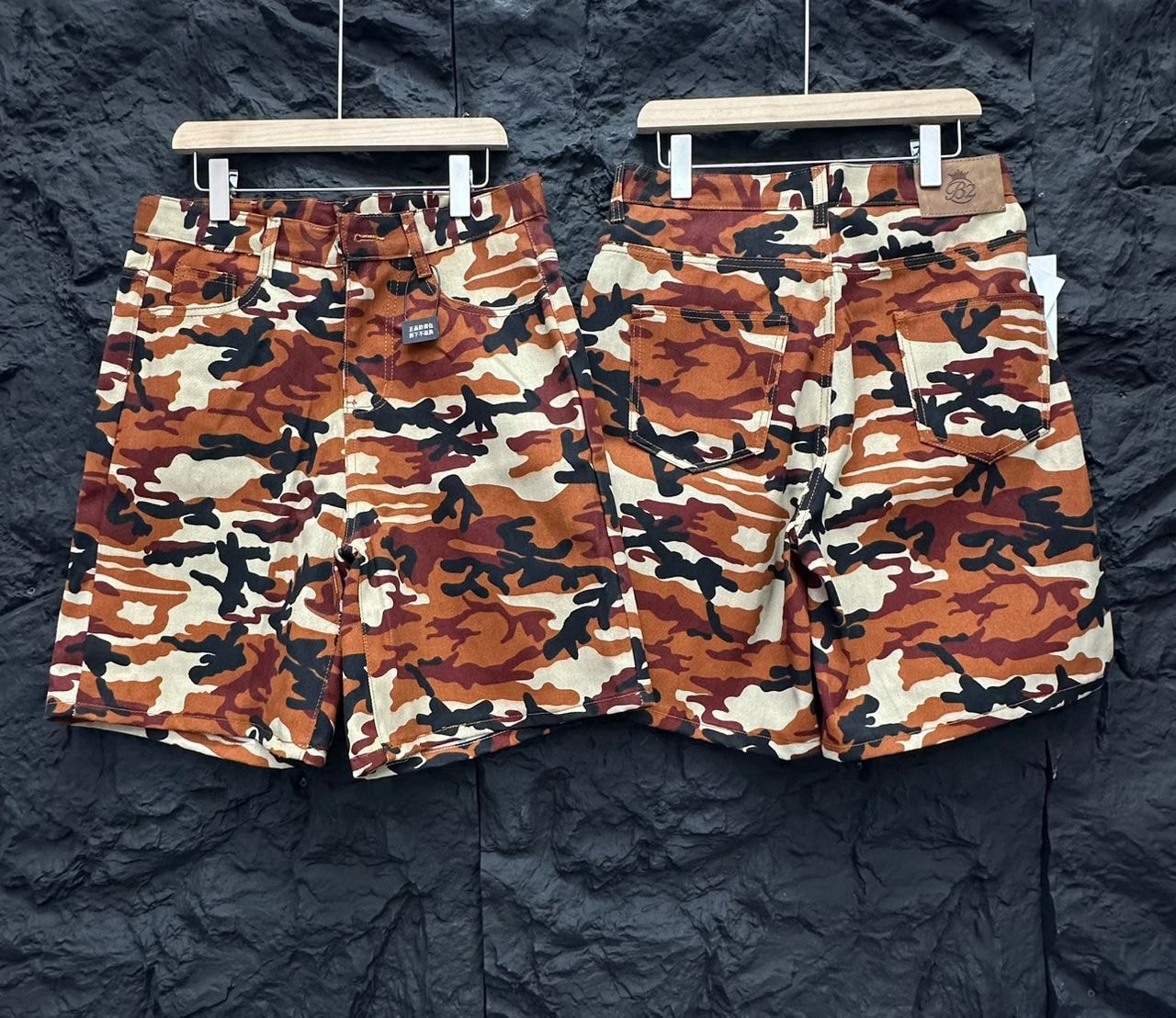 Front and back views of orange brown black camouflage shorts with pockets and leather waistband patch.