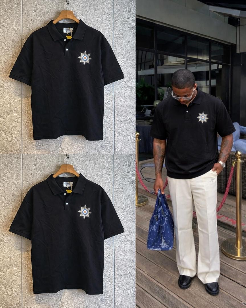 Black polo shirt with star embroidery displayed in flat lay and worn by a model with white trousers.