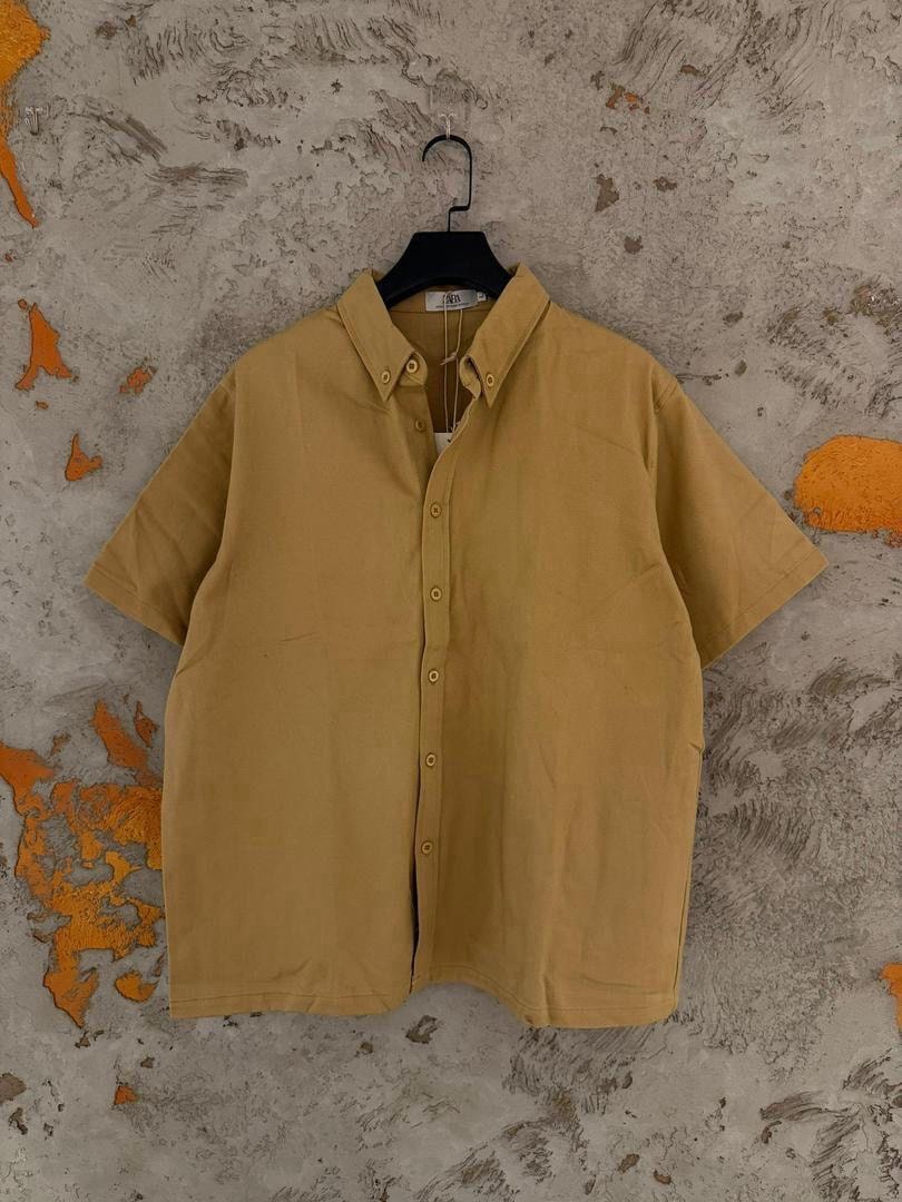 Yellow short sleeve button-up shirt hanging on hanger against textured wall.