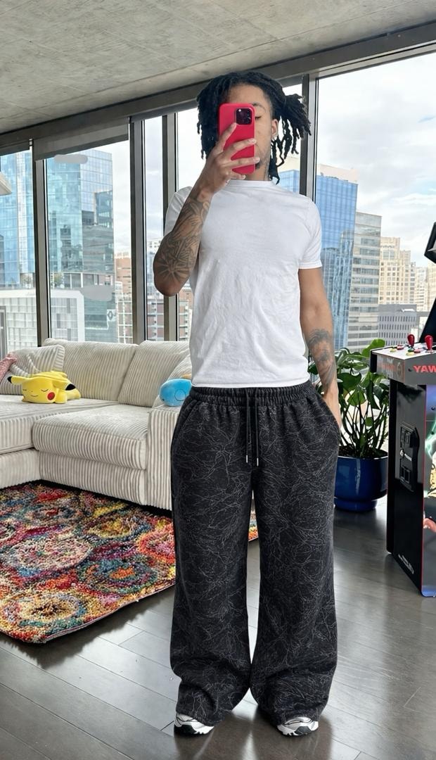 Model wearing black cracked-pattern wide-leg joggers with white t-shirt in modern apartment.