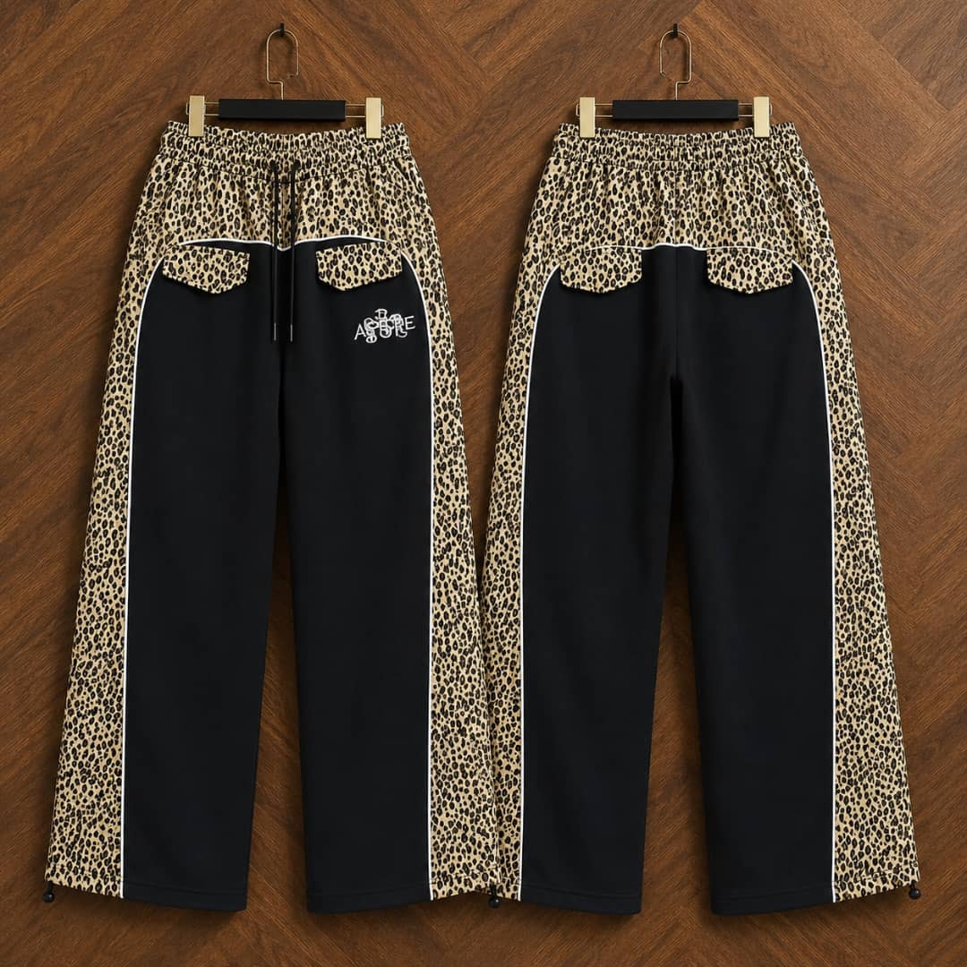 Black AFRORE leopard print joggers hanging on wooden background, front and back views.